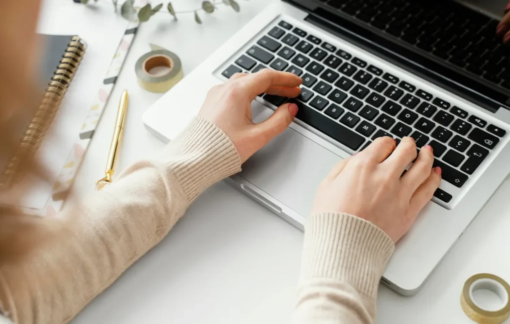Person typing on a laptop with writing tools and notebook on a desk – representing how to get paid to write online through freelance work from home.
