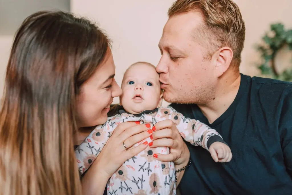 Young couple lovingly holding and kissing their baby at home, symbolizing the emotional and financial risks new parents face in today's world.
