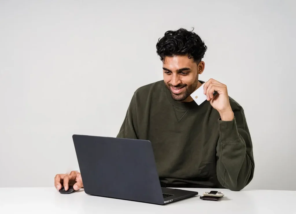 Man holding a credit card while managing payments on a laptop, representing smart strategies to pay off credit card debt efficiently online.