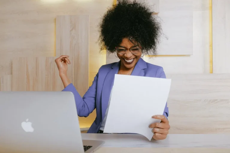 Smiling woman reviewing financial documents at her desk with a laptop