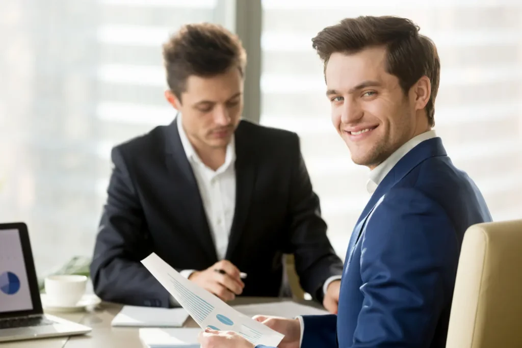 Young professional smiling while holding financial report during a discussion about smart ways to invest in a modern office.