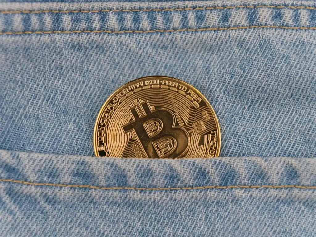 Gold Bitcoin coin tucked into the pocket of blue denim jeans, symbolizing how to store cryptocurrency securely in everyday life.