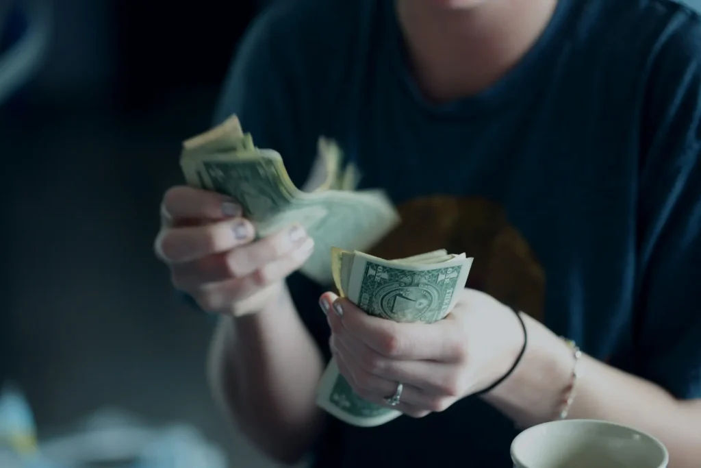Person counting U.S. dollar bills at home, symbolizing how to make money without a job through personal income or side hustle earnings.