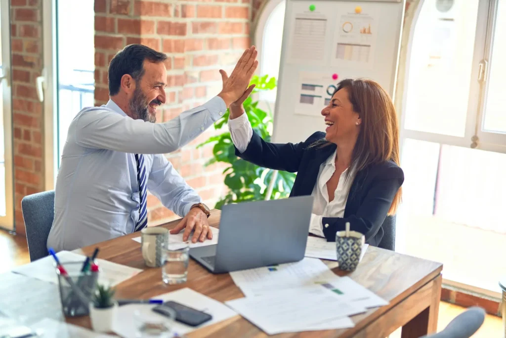 Two business professionals celebrating success with a high-five in a modern office setting after taking steps to start a business in the U.S.