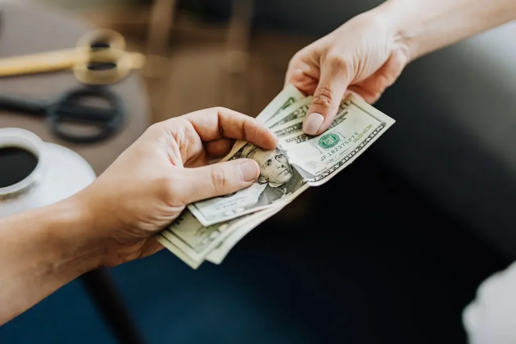 Close-up of one person handing U.S. dollar bills to another person indoors, illustrating a loan without income verification.