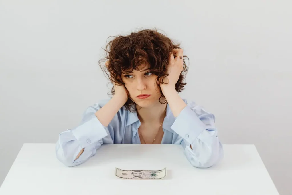 Worried young woman looking at a five-dollar bill on a table, symbolizing financial stress and uncertainty while trying to understand what is a recession.