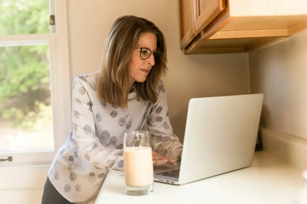 Middle-aged woman working on a 10-year retirement plan using her laptop in the kitchen.
