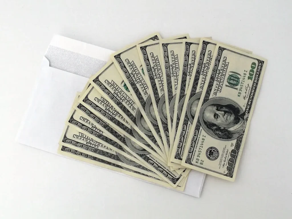 Stack of $100 U.S. bills fanned out over a white envelope on a white background, symbolizing income from things you can rent out.
