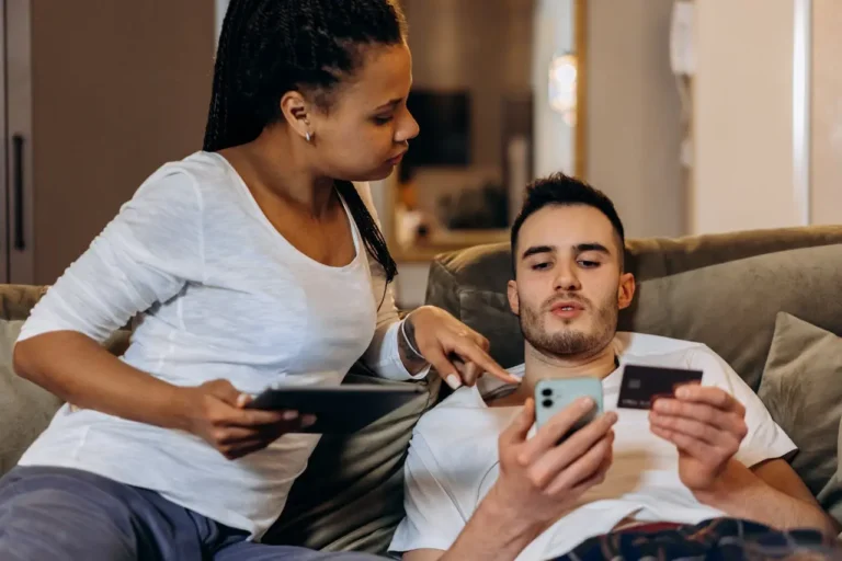 Young couple reviewing credit card information together on a smartphone and tablet at home