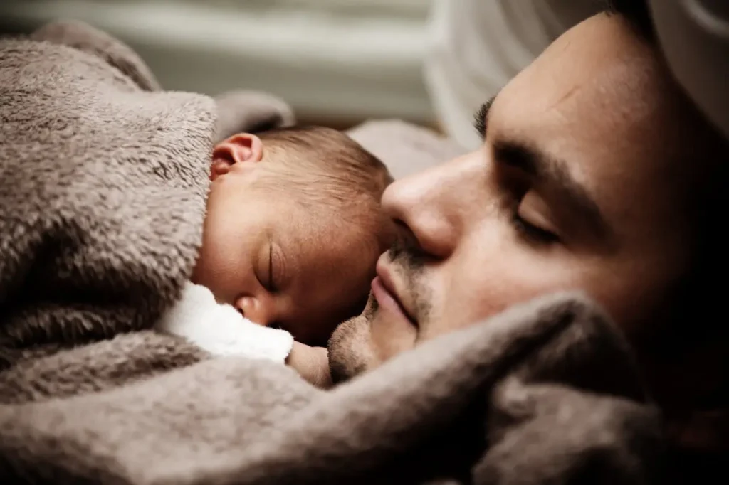 Father and newborn baby peacefully sleeping under a blanket, symbolizing the protection and security offered by life insurance.