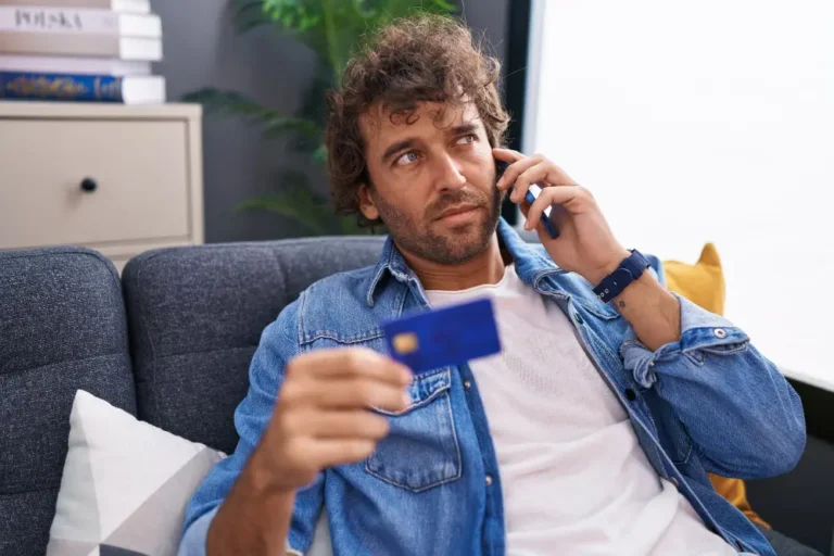 Concerned man on phone holding credit card while reporting suspected fraud and discussing credit card fraud liability.