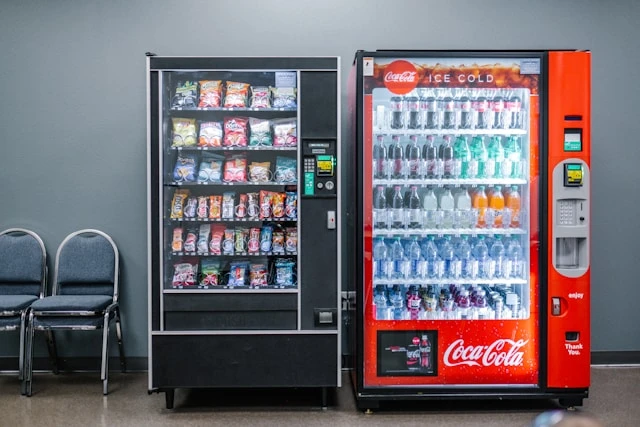 Snack and beverage vending machines placed side by side in a public waiting area, illustrating passive income ideas through automated sales.