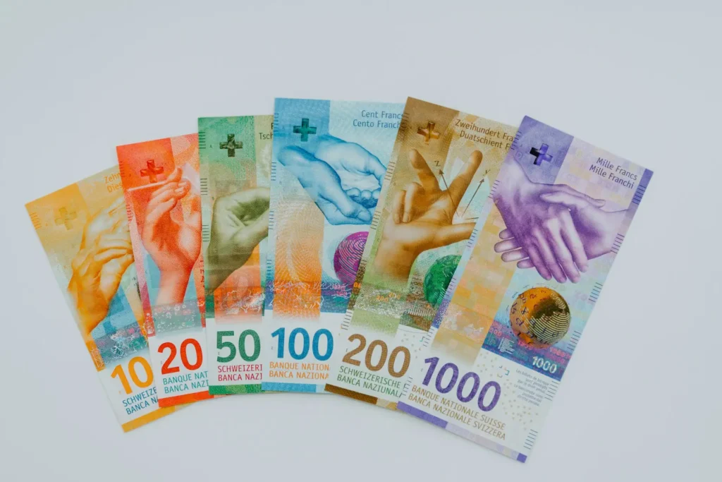 Colorful Swiss franc banknotes in various denominations arranged in a fan shape on a white background, symbolizing Swiss franc investment opportunities.