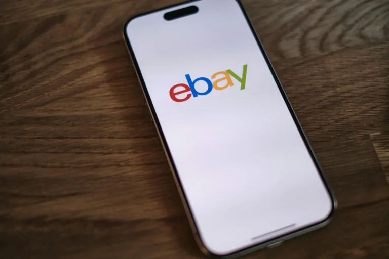 Smartphone displaying eBay logo on screen, placed on a wooden surface.