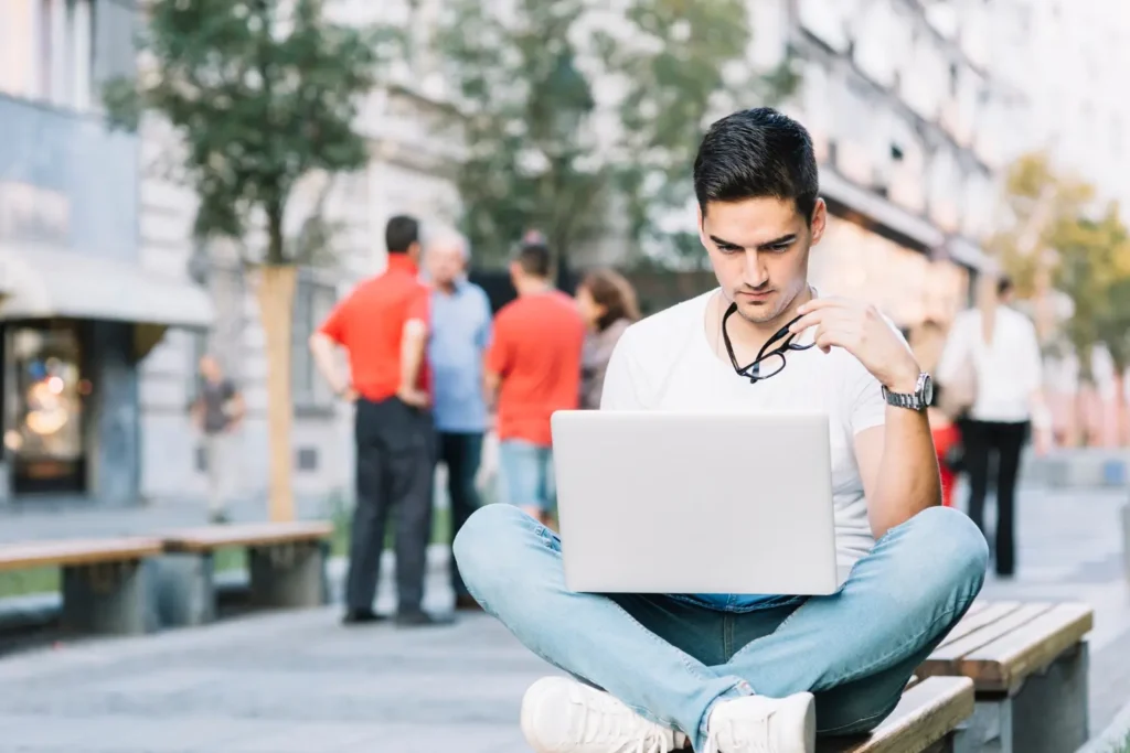 Young man researching student loan payments and relief options on a laptop in an urban setting.