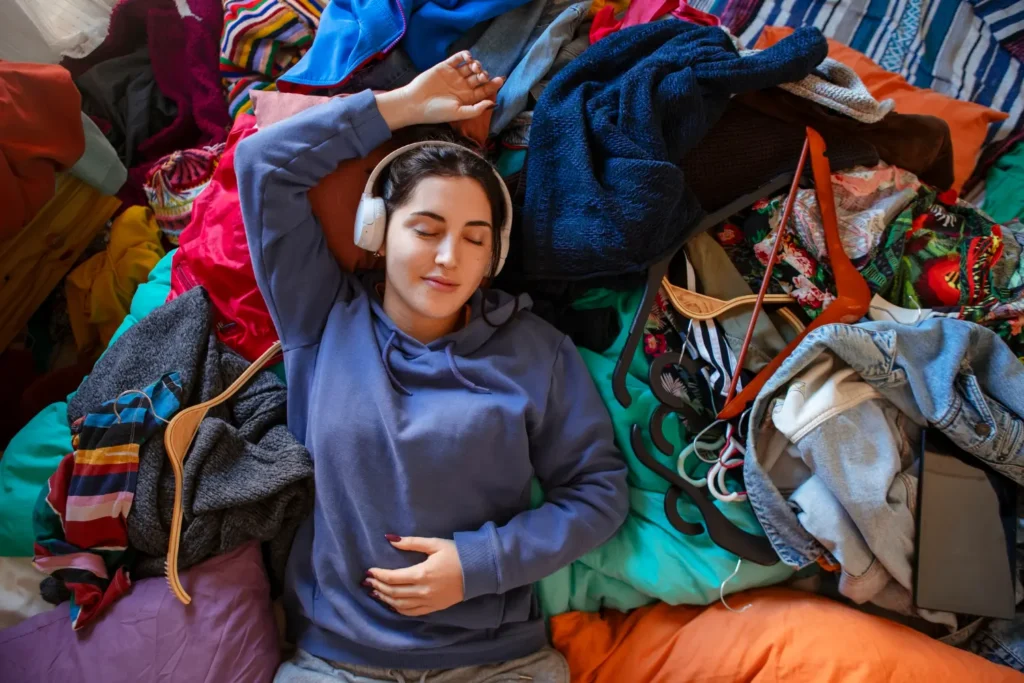 Woman relaxing on a pile of clothes after closet clean-out, preparing to sell used clothes at the best places to sell used clothes for cash in 2025.